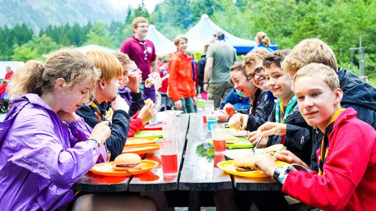 Scout group eating outside at a table while on camp
