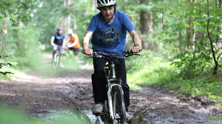 Young boys cycling through a muddy puddle in a forest