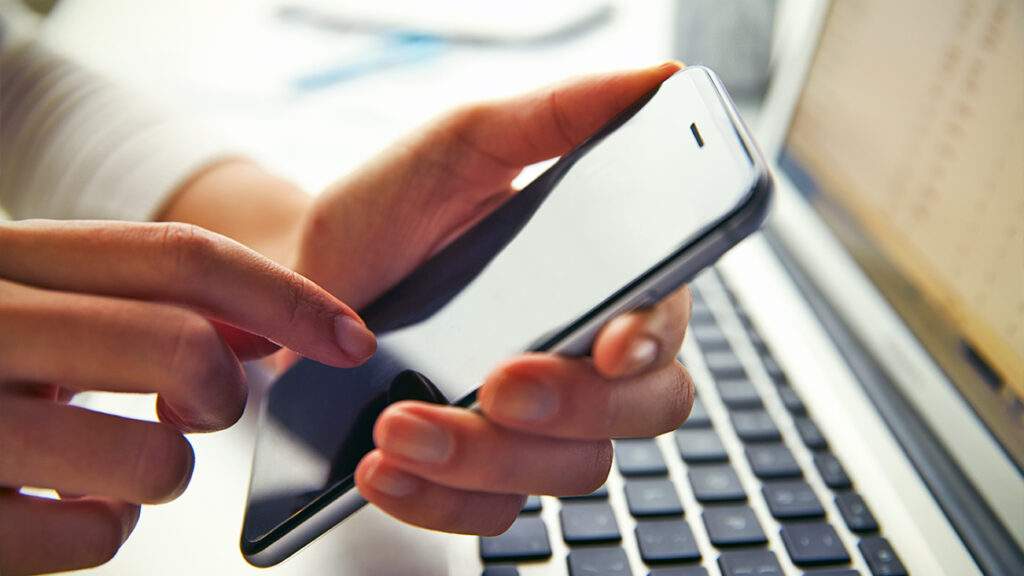 Person using a smart phone while on their computer