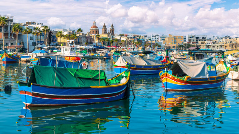 Landscape with traditional Luzzu boat in harbor of Marsaxlokk, Malta. Picturesque fishing village with colorful traditional Luzzu boats in Marsaxlokk, Malta