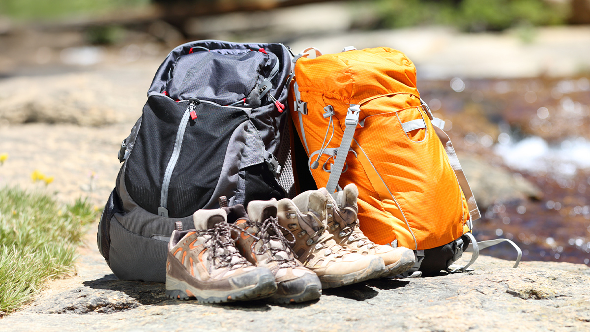 black and orange backpacks on rocky floor behind hiking shoes